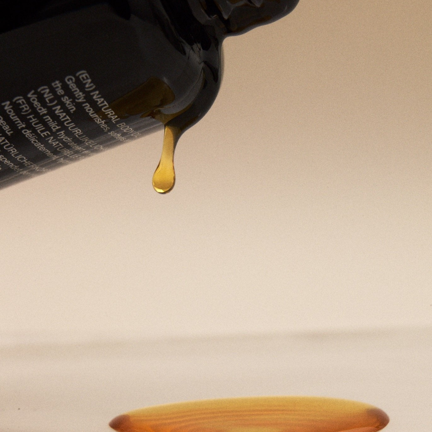 Una gota de aceite corporal cae lentamente, mostrando su textura fluida y luminosa antes de la aplicación.