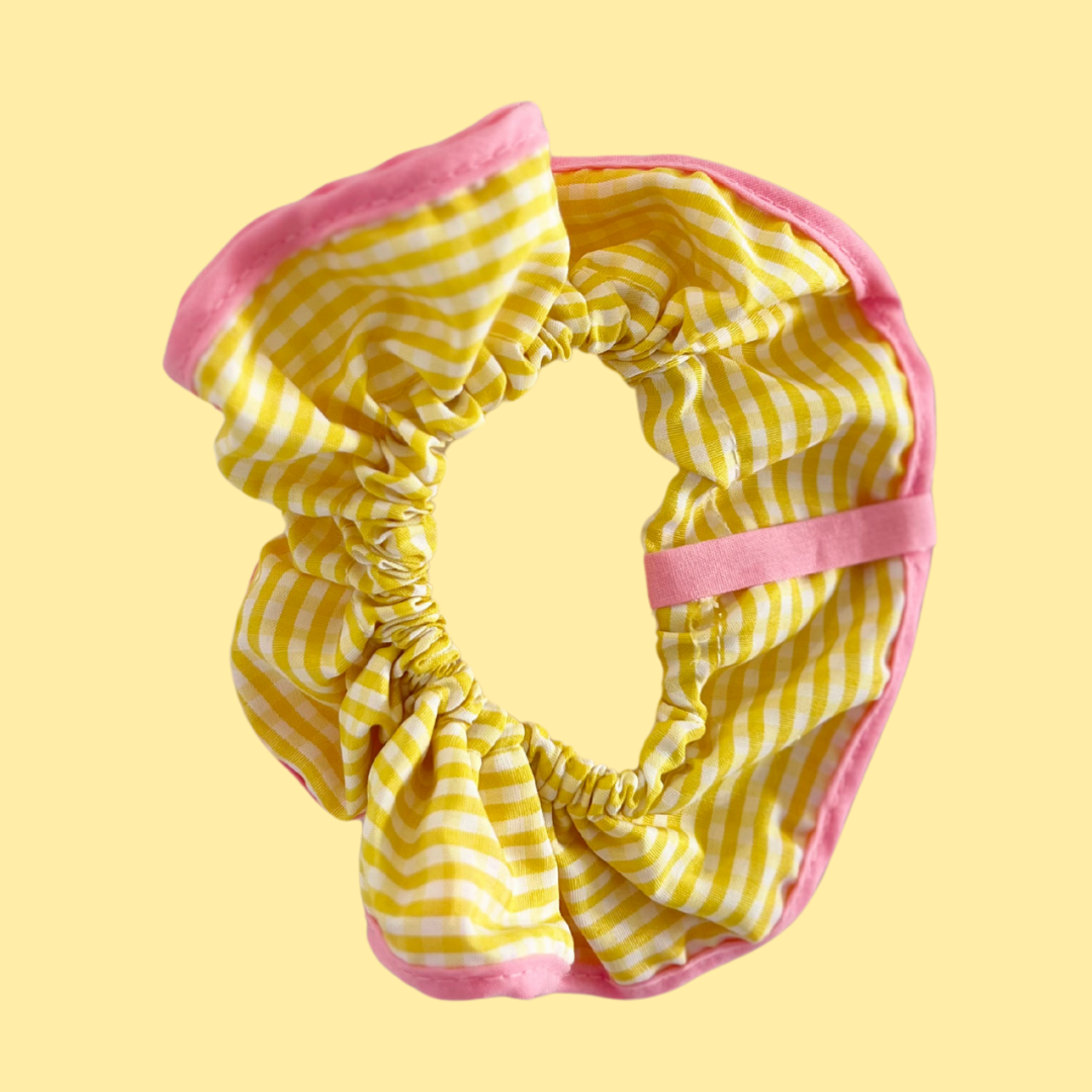 Coletero scrunchie para pelo rebelde de La Crème Organics. Decorado con cuadros amarillos y remate rosa perfecto para la primavera.