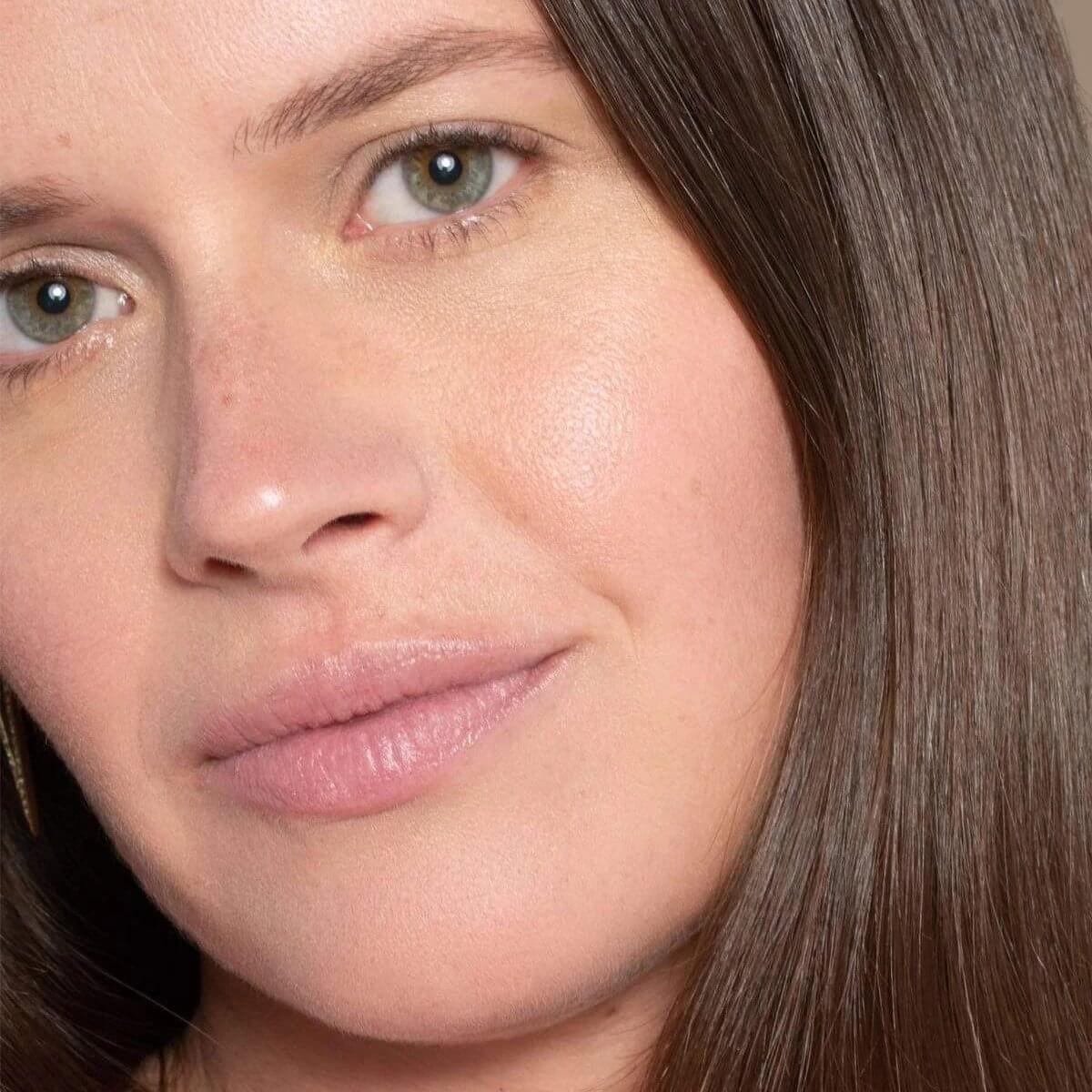 El corrector ILIA en tono 'Kava SC3' aplicado sobre piel media; la modelo sonríe mostrando un acabado suave y uniforme.