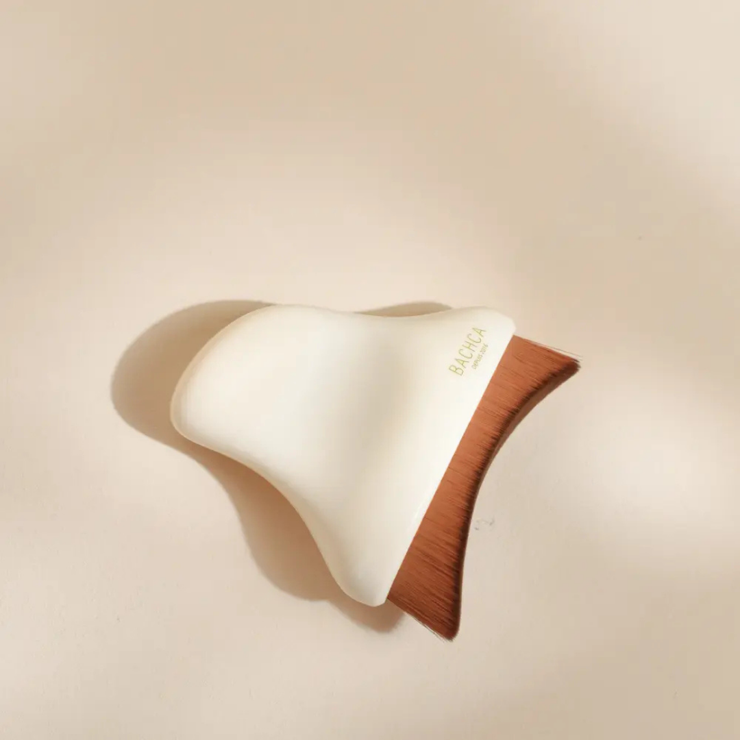 Cepillo facial de drenaje linfático Bachca con fibras densas y forma ergonómica para el rostro.