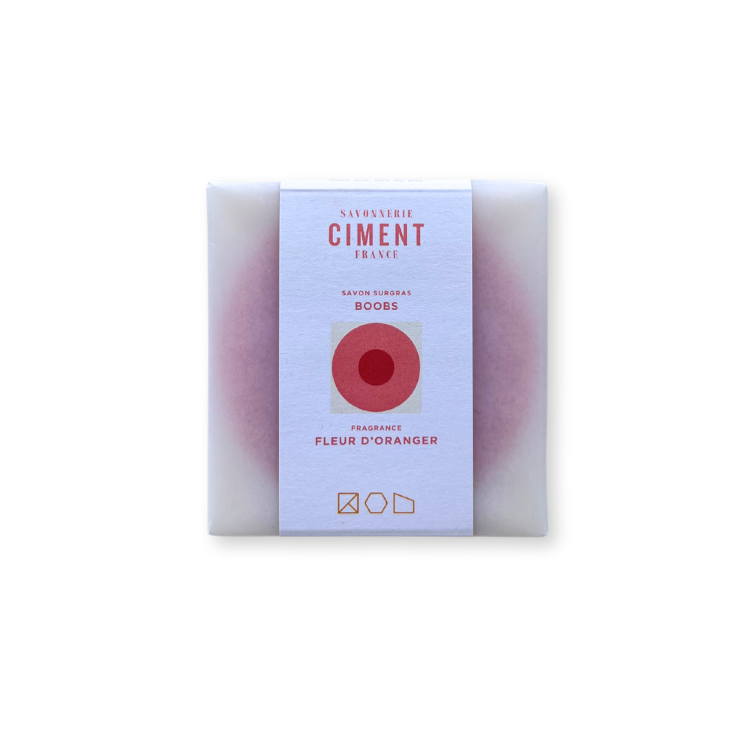 Savon Boobs de Ciment Paris con su envoltorio. Jabón sólido ecológico con forma artística y aroma natural a flor de azahar.